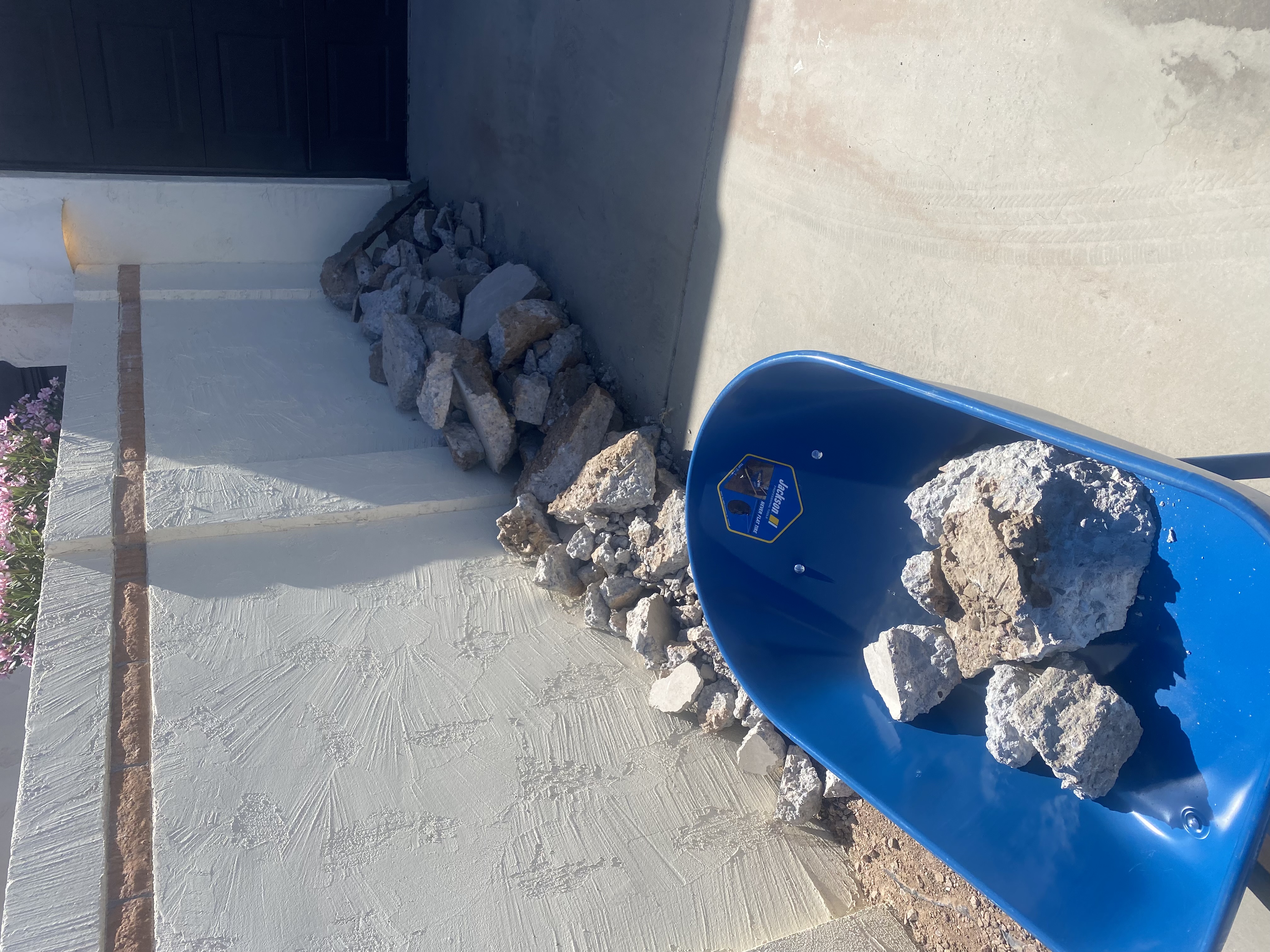 Broken concrete loaded into a wheelbarrow beside a staged rubble pile