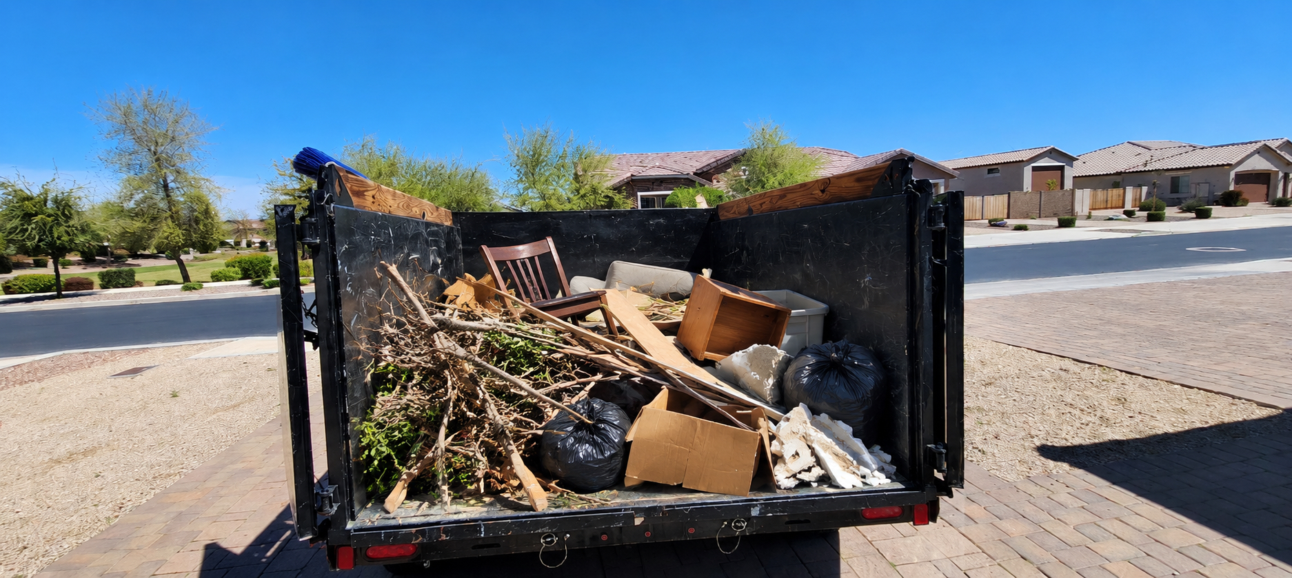 Dump trailer about half full of branches, a chair, boxes, and bags