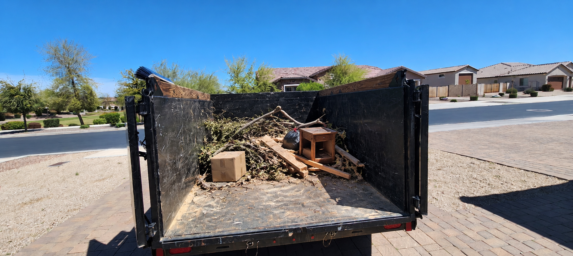 Dump trailer about a quarter full with a nightstand, box, and brush