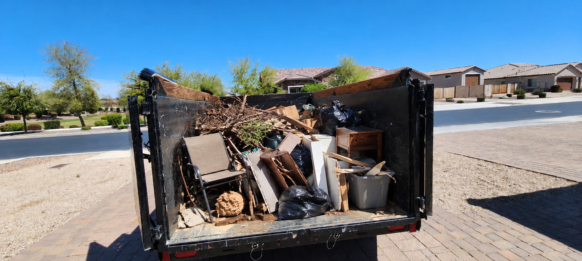 Dump trailer about three-quarters full of furniture, bags, and yard brush